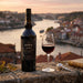 Bottle of Dow's 2020 Port wine with a glass on a ledge overlooking a river and cityscape.