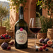 A bottle of Ferreira Porto Ruby Port stands on a wooden table beside a filled wine glass, surrounded by figs, cherries, and berries in an outdoor patio setting.
