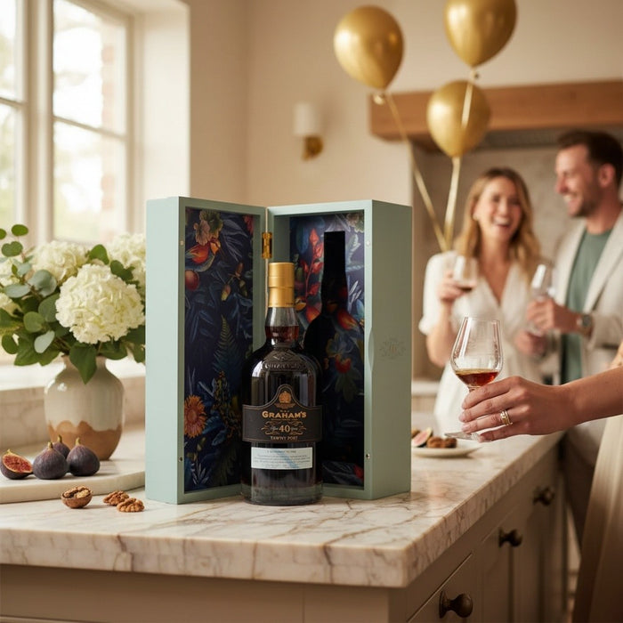Bottle of Graham's 40 year old port in a decorative box on a kitchen counter with people in the background.