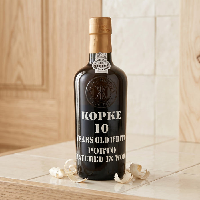 Kopke 10 Years Old White Porto bottle on a wooden surface with a tiled wall background
