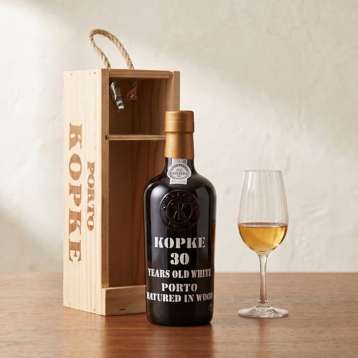 Kopke 30 years old white porto bottle with wooden box and glass of wine on a table.
