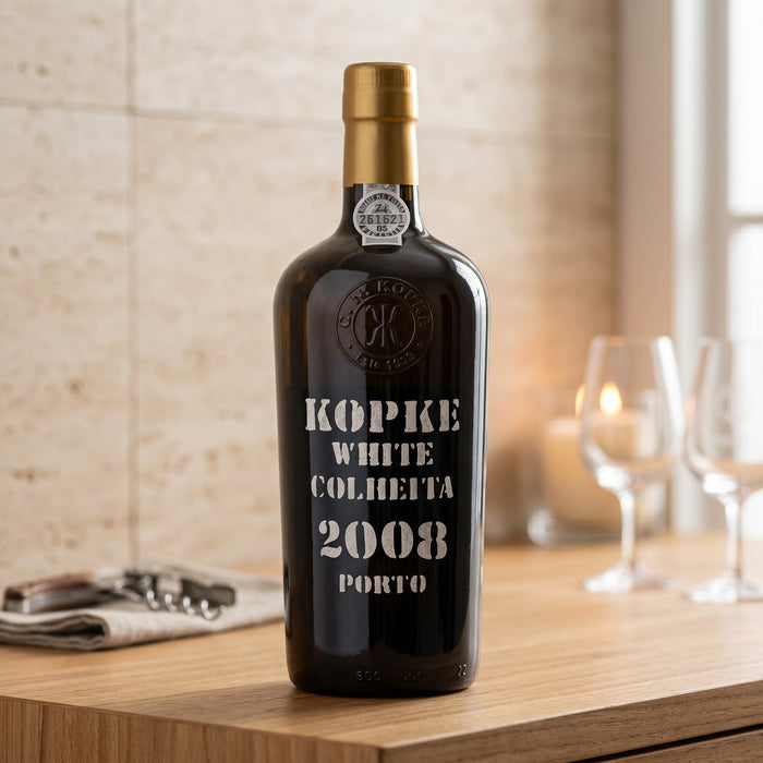 Bottle of Kopke White Colheita 2008 Porto wine on a wooden table with glasses in the background.