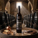 A bottle of Sandeman Royal Ambrosante Pedro Ximenez 20 Year Old Sherry stands on a wooden barrel in a stone whisky cellar, surrounded by a wine glass, cheese, nuts, and a leather journal.