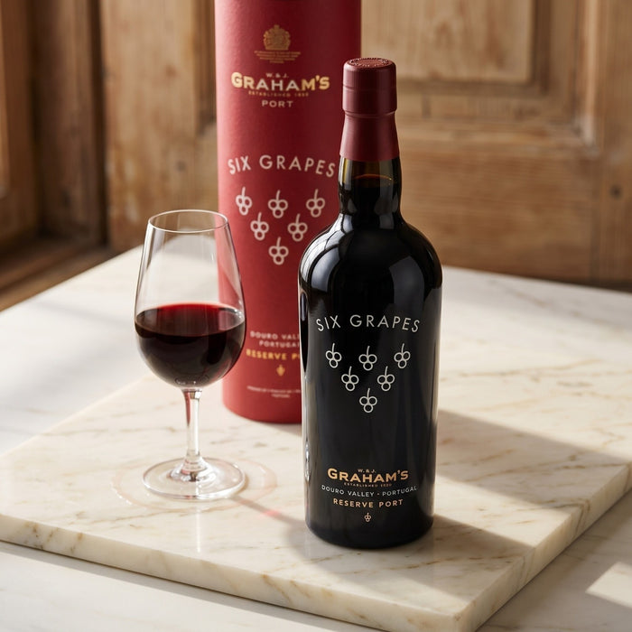 Bottle and glass of Graham's Six Grapes Reserve Port on a marble surface with wooden background
