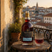 A bottle of Graham's 40 Tawny Port sits on a round wooden table next to a cut glass filled with the amber liquid, set against a scenic background of a European city skyline at sunset.