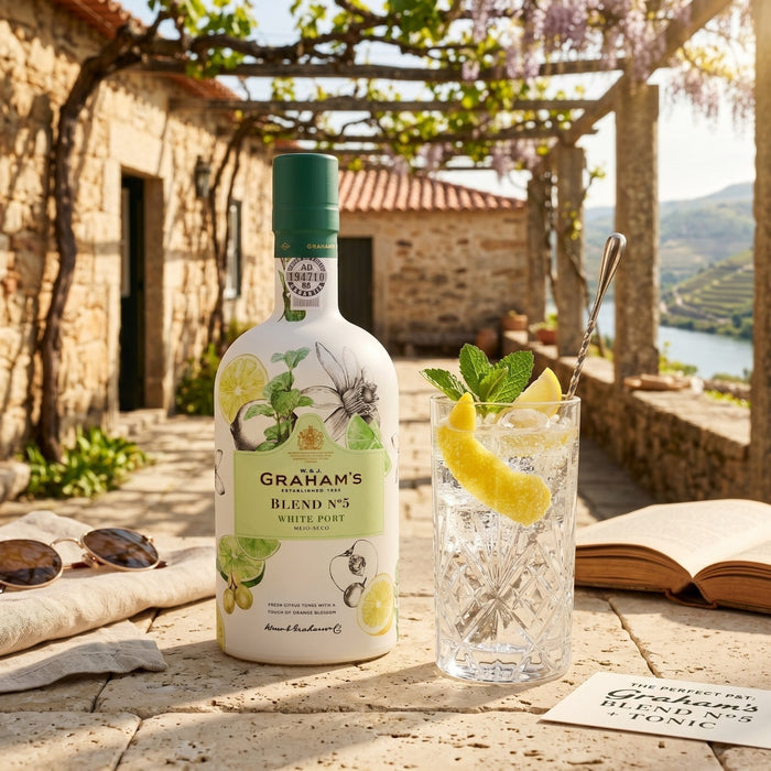 Bottle of Graham's Blend No.5 White Port with a glass of port and lemon garnish on a stone patio.