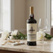 Sandeeman wine bottle on a table with a glass and flowers in the background